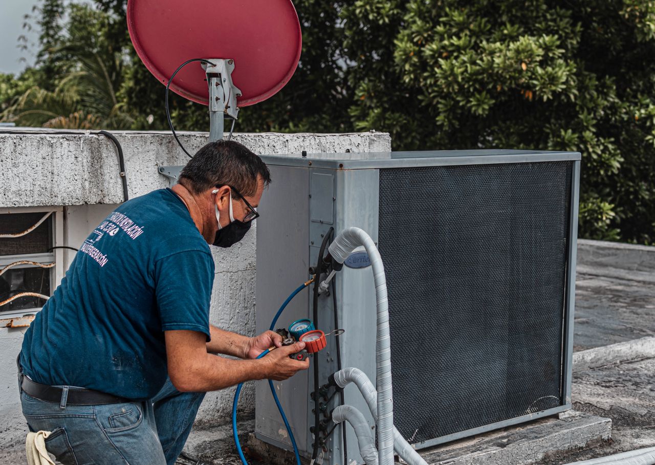 services-01 Technician repairing an air conditioner unit outdoors, wearing a facemask and using a manifold gauge.